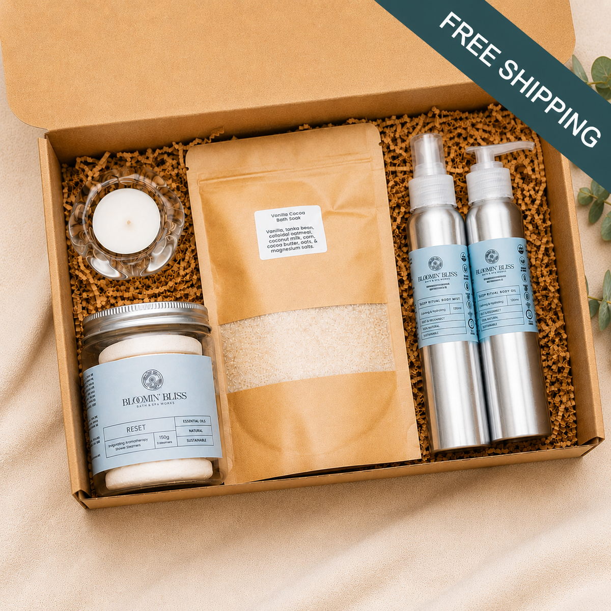 An open kraft gift box filled with spa-style products on a soft beige fabric background. The set includes two silver bottles, one with body oil and one with a body mist, a tan bath salt stand-up pouch with a clear window, a glass jar filled with five aromatherapy shower steamers, and a small glass candle holder with tea light candle inside. Subscription box Canada. 