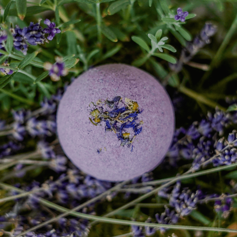 A lavender bath bomb with floral patterns on its surface, placed on a bed of fresh lavender flowers.