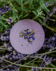 A lavender bath bomb with floral patterns on its surface, placed on a bed of fresh lavender flowers.