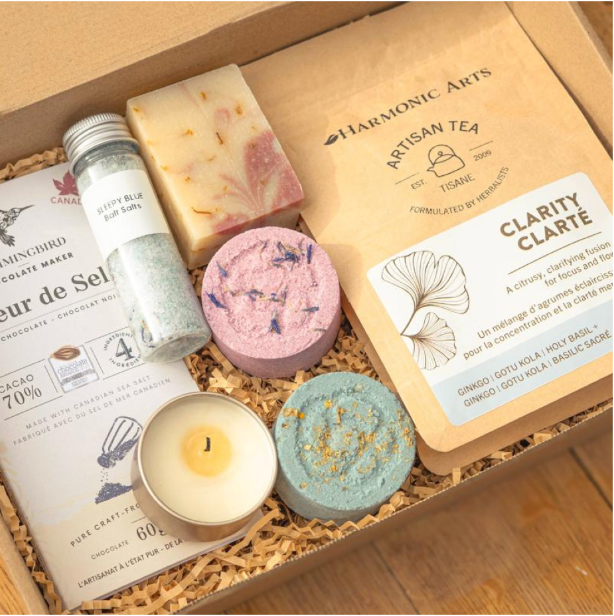 Bloom Box contents including bath salts, aromatherapy soap, a massage candle, bath bombs, chocolate, and tea arranged in a gift box