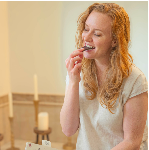 Woman eating a piece of chocolate in a softly lit room from a self care subscription box Canada
